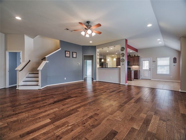 Unfurnished living room with ceiling fan, wood finished floors, baseboards, vaulted ceiling, and stairway | Image 17