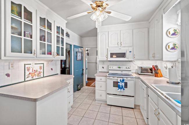 Kitchen featuring white appliances, backsplash, a ceiling fan, and light tile patterned floors | Image 5
