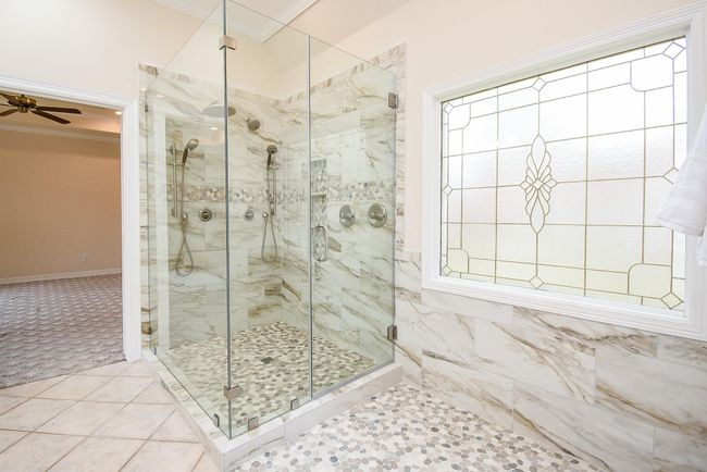 This bathroom features a spacious, glass-enclosed shower with elegant marble-style tiles and a decorative stained glass window, offering a luxurious and bright atmosphere. | Image 4