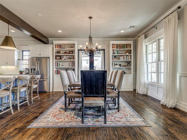 Dining area with a notable chandelier, a decorative wall, dark wood-style flooring, beamed ceiling, and crown molding | Image 11