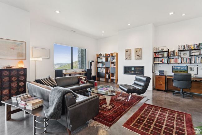 Living area featuring concrete floors, a glass covered fireplace, recessed lighting, and built in desk | Image 54