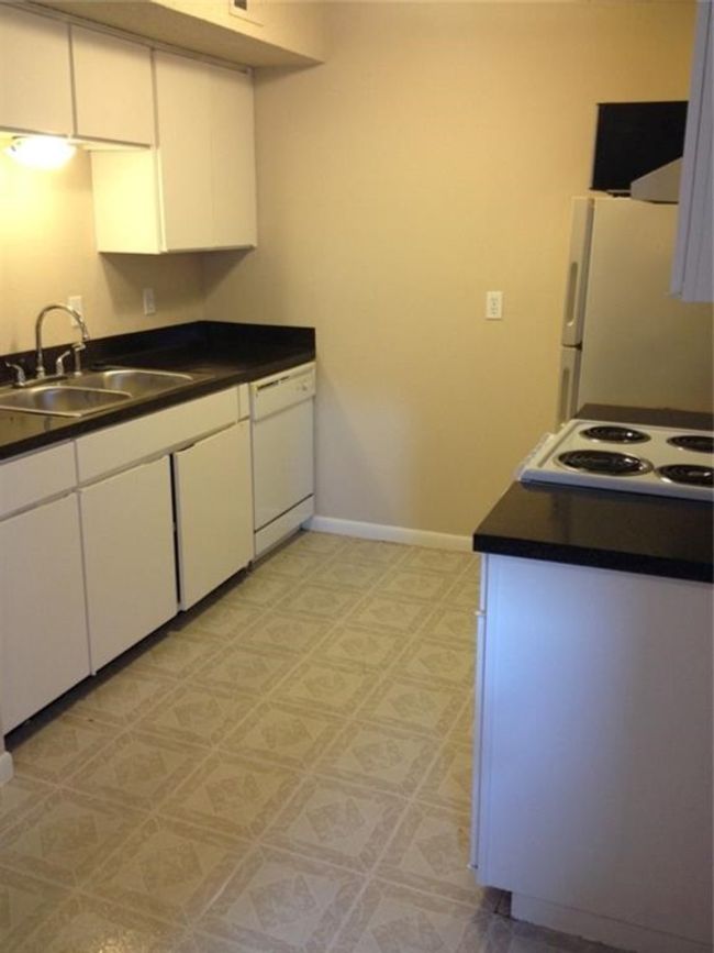 Kitchen featuring white cabinetry, white appliances, dark countertops, and a sink | Image 9