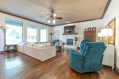 Living room featuring ceiling fan, crown molding, dark wood-type flooring, and a stone fireplace | Image 3