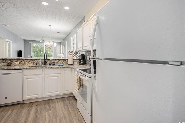 Kitchen with white appliances, light wood-style flooring, white cabinets, a chandelier, and light stone countertops | Image 11