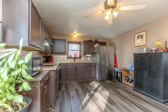 Kitchen with ceiling fan, freestanding refrigerator, under cabinet range hood, dark wood finished floors, and decorative backsplash | Image 12