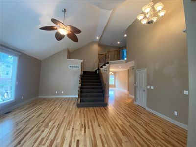 Unfurnished living room with high vaulted ceiling, light hardwood / wood-style floors, and ceiling fan with notable chandelier | Image 3