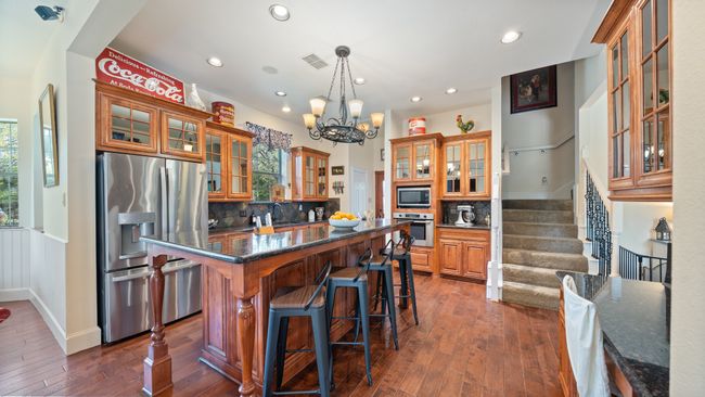 Kitchen featuring a breakfast bar, stainless steel appliances, a kitchen island, glass insert cabinets, and brown cabinetry | Image 8