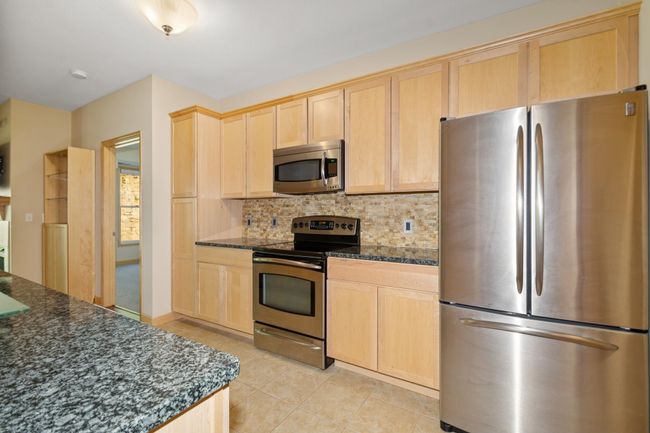 The kitchen comes fully equipped with granite countertops, rich maple cabinetry, tile backsplash, stainless steel appliances, and a spacious center island, perfect for meal prep and casual dining. | Image 5