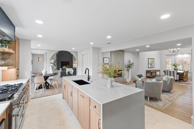 Kitchen featuring a warm lit fireplace, open floor plan, light brown cabinetry, recessed lighting, and a kitchen island with sink | Image 17