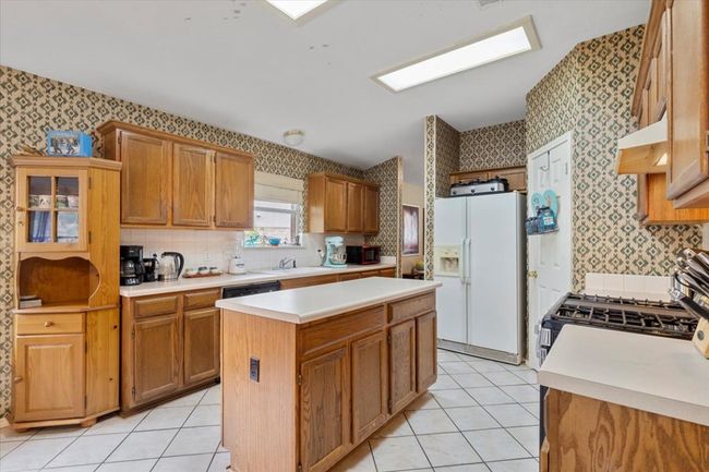Kitchen with white fridge with ice dispenser, wallpapered walls, black microwave, under cabinet range hood, and light countertops | Image 10