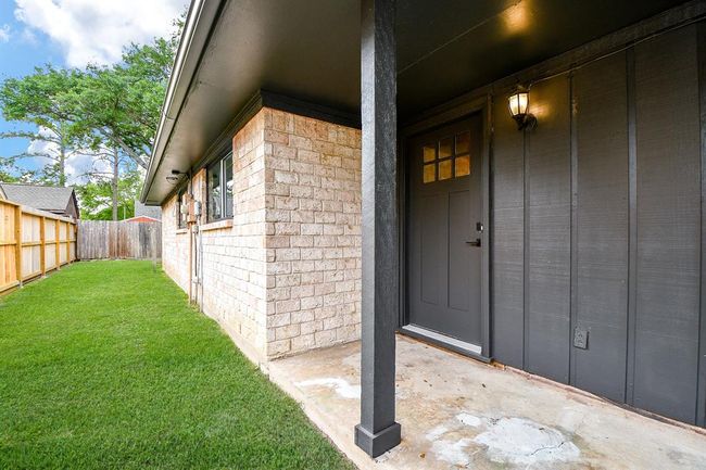 This photo shows a cozy entrance to a brick house with a modern black door and light fixture. There's a small, well-maintained front porch and a fenced yard with green grass, offering privacy and outdoor space. | Image 44
