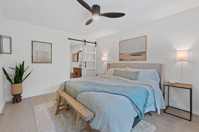 Bedroom with a barn door, light wood-type flooring, connected bathroom, and ceiling fan | Image 18