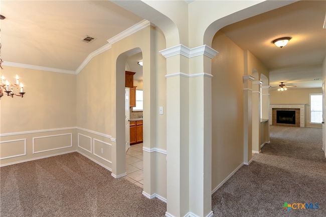 Entry way showing the formal dining looking into the kitchen. Hallway leading to the living room with fireplace. Crown molding and archways give this home an inviting feel. | Image 5