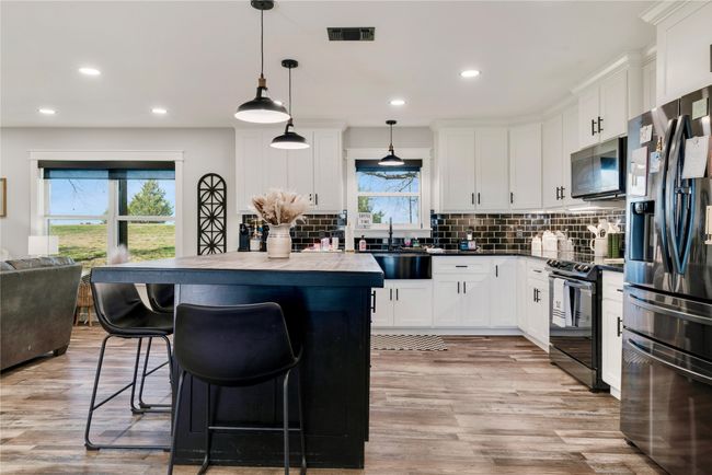 Kitchen featuring a kitchen island, stainless steel fridge with ice dispenser, a breakfast bar area, visible vents, and black / electric stove | Image 7