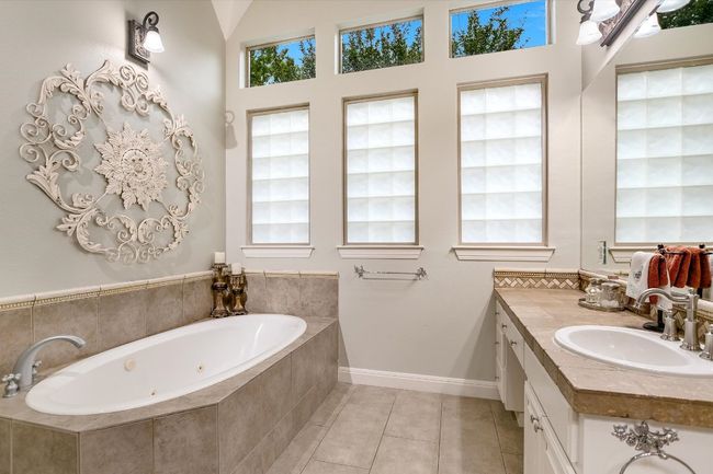 Luxury bath with jetted tub, tile patterned flooring, and vanity with dressing table. | Image 16