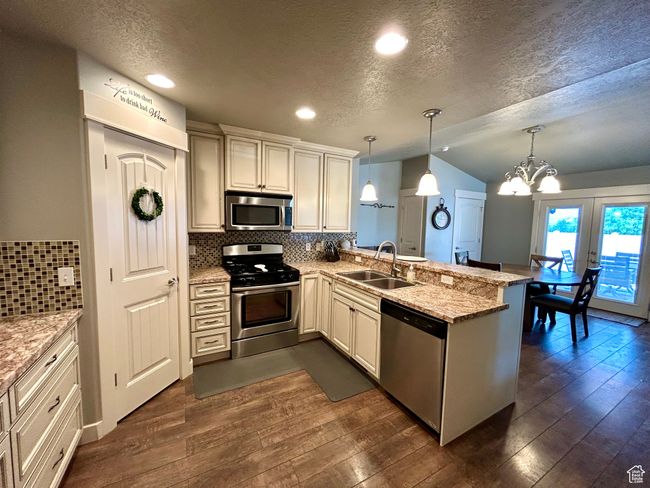 Kitchen with appliances with stainless steel finishes, a sink, a peninsula, a textured ceiling, and vaulted ceiling | Image 11
