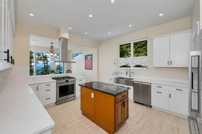 Kitchen featuring stainless steel gas range oven, exhaust hood, a chandelier, a kitchen island, and white cabinets | Image 8