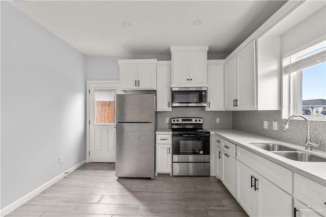 Kitchen featuring appliances with stainless steel finishes, a sink, decorative backsplash, and white cabinetry | Image 10