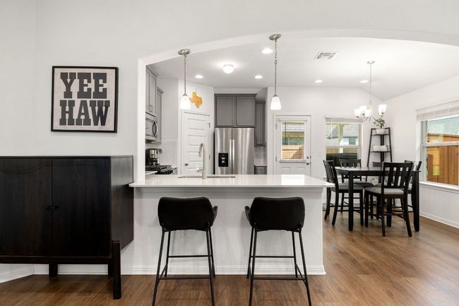 Kitchen with light countertops, a kitchen bar, appliances with stainless steel finishes, a peninsula, and dark wood-style floors | Image 9