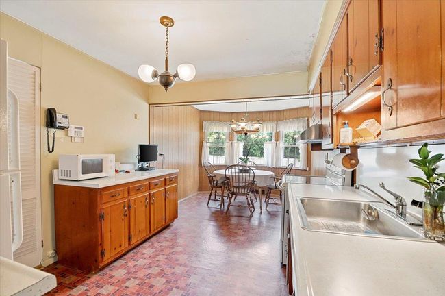 Kitchen with white microwave, a chandelier, range, brown cabinets, and light countertops | Image 9