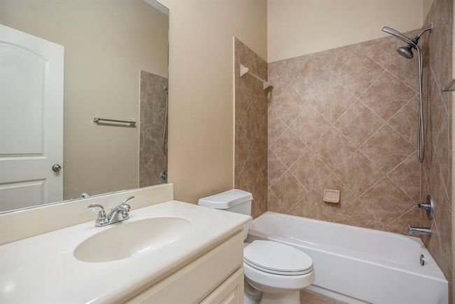 Located next to the third secondary bedroom, this full bathroom features a tiled tub/shower combo, a large vanity with under-sink storage, and a wide mirror for added convenience. Neutral finishes and classic design make it both functional and easy to personalize. | Image 27