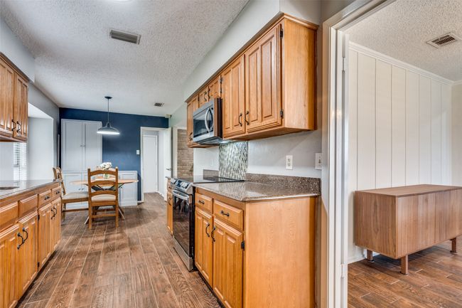 Kitchen featuring appliances with stainless steel finishes, a textured ceiling, dark wood-style floors, brown cabinetry, and decorative light fixtures | Image 14