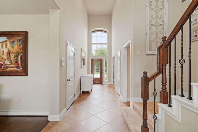 This inviting entryway features high ceilings and large windows that let in natural light. The space is accented with elegant tile flooring and a stylish staircase with wooden railings. | Image 6