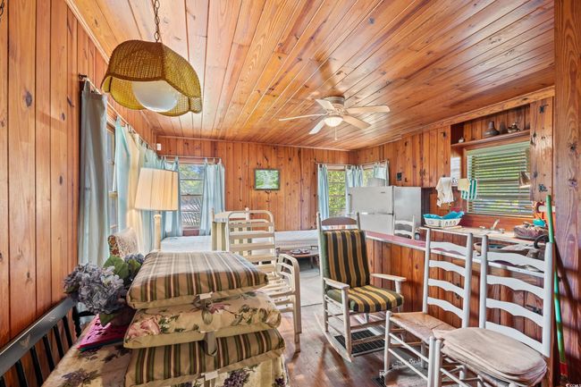 Kitchen with wooden ceiling, wooden walls, freestanding refrigerator, a ceiling fan, and wood finished floors | Image 15