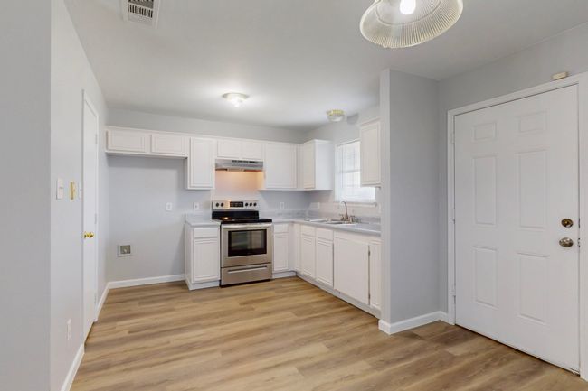 Kitchen with stainless steel range with electric stovetop, a sink, under cabinet range hood, baseboards, and white cabinets | Image 25