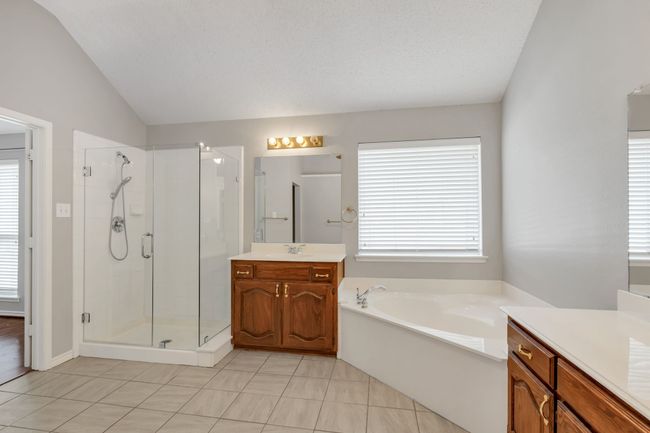 Primary bath featuring a garden tub, a shower, vaulted ceiling, and separate vanities | Image 25
