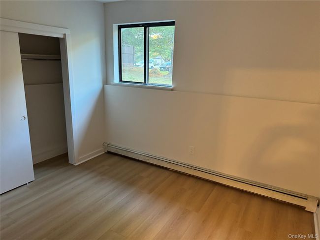 Unfurnished bedroom with a baseboard heating unit and light wood-style floors | Image 4