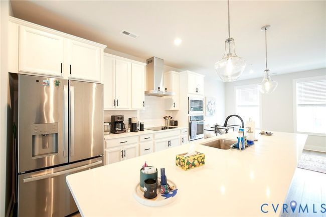 Kitchen with stainless steel appliances, an island with sink, decorative backsplash, wall chimney exhaust hood, and white cabinets | Image 39