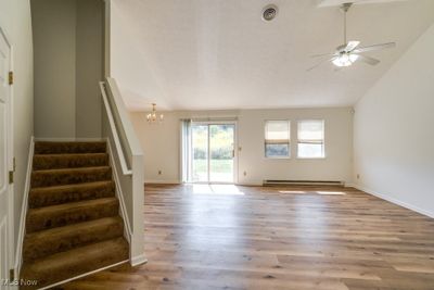 Unfurnished living room featuring ceiling fan with notable chandelier, high vaulted ceiling, light hardwood / wood-style flooring, and a baseboard radiator | Image 3