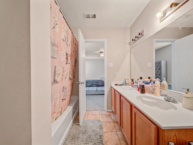Ensuite bathroom with double vanity, a ceiling fan, tile patterned flooring, and shower / bath combination with curtain | Image 12