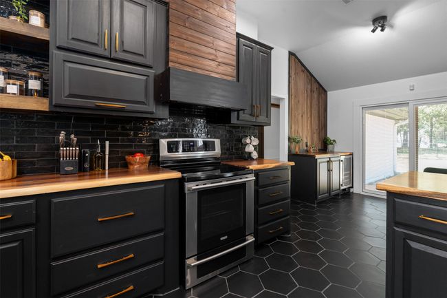 Kitchen with lofted ceiling, stainless steel range with electric stovetop, dark tile patterned floors, range hood, and backsplash | Image 7
