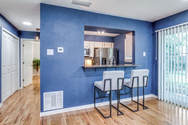 Kitchen with appliances with stainless steel finishes, a breakfast bar, white cabinetry, light wood-style flooring, and a textured wall | Image 4