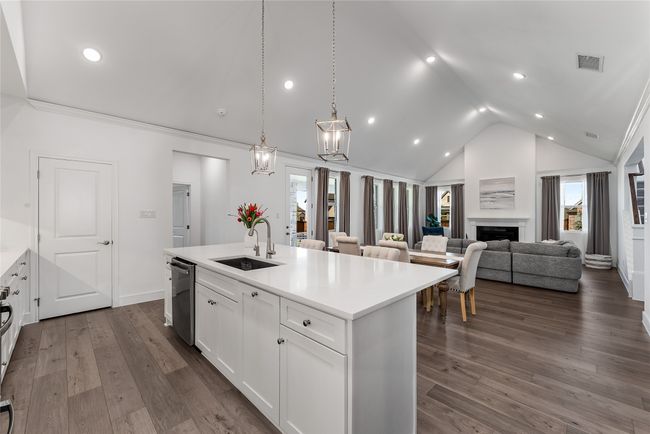 Kitchen with lofted ceiling, stainless steel dishwasher, a center island with sink, white cabinets, and a fireplace | Image 9