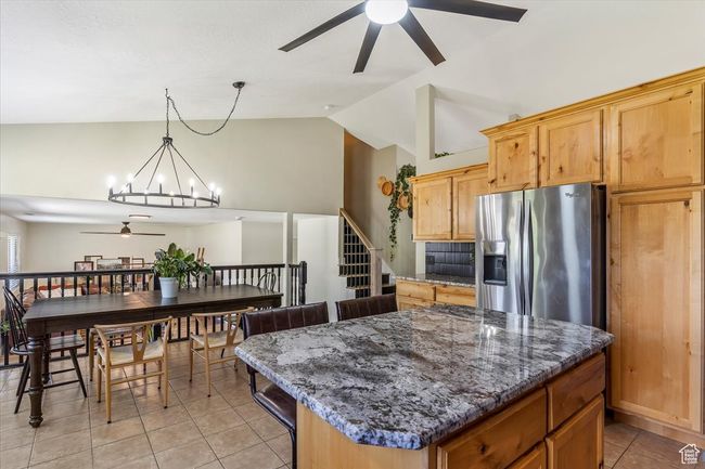 Kitchen featuring a ceiling fan, stainless steel refrigerator with ice dispenser, light tile patterned floors, vaulted ceiling, and a chandelier | Image 8