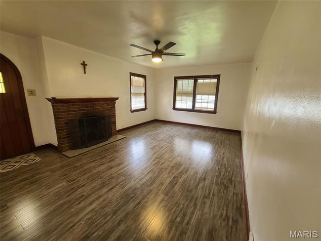 Unfurnished living room featuring arched walkways, a ceiling fan, dark wood finished floors, and a brick fireplace | Image 7
