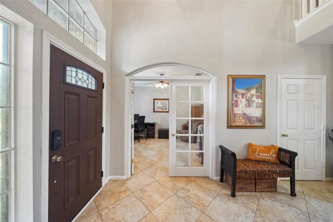 This inviting entryway features a dark wood front door with decorative glass, tile flooring, and abundant natural light. A set of French doors leads to a cozy office space. | Image 4
