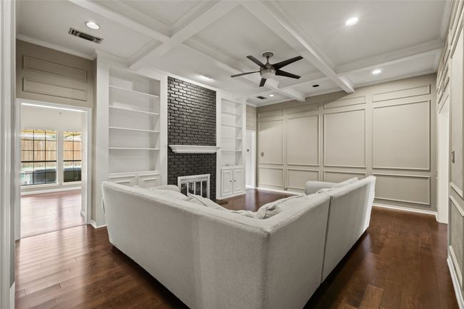 Living area featuring a decorative wall, a ceiling fan, dark wood finished floors, beam ceiling, and built in shelves | Image 13