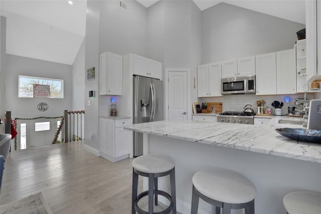 Kitchen featuring white cabinets, light stone counters, high vaulted ceiling, and stainless steel appliances | Image 5