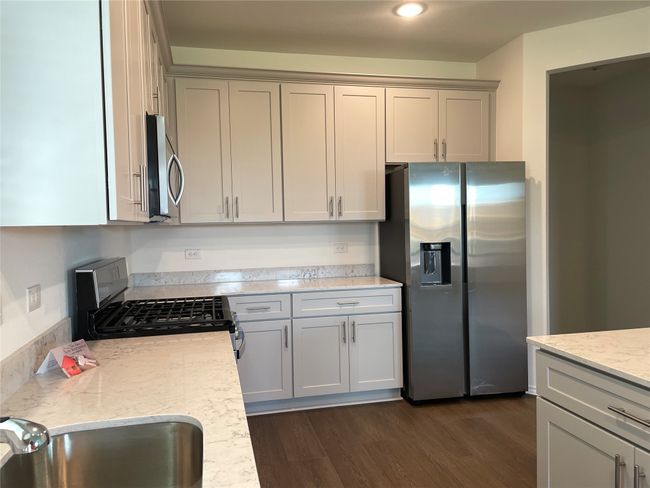 Kitchen featuring appliances with stainless steel finishes, a sink, dark wood-style floors, light stone countertops, and gray cabinetry | Image 4