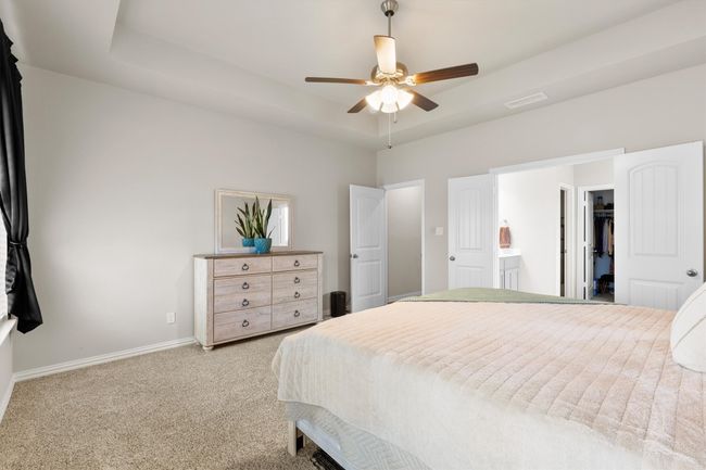 Bedroom with light colored carpet, a tray ceiling, a spacious closet, a ceiling fan, and connected bathroom | Image 21