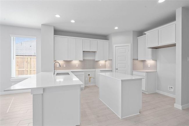 This kitchen is by far any chef’s dream! This spacious kitchen features high ceilings, stained wood cabinets, quartz countertops, modern tile backsplash, recessed lighting, under cabinet lighting, island, extended countertop for breakfast bar, and a walk-in pantry all overlooking your huge family room. | Image 5