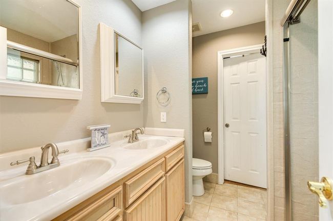 This bathroom features a dual-sink vanity with elegant fixtures, a large mirror, and ample storage. Neutral tones create a calming atmosphere, while the tiled floor and shower enclosure add a touch of luxury. | Image 15