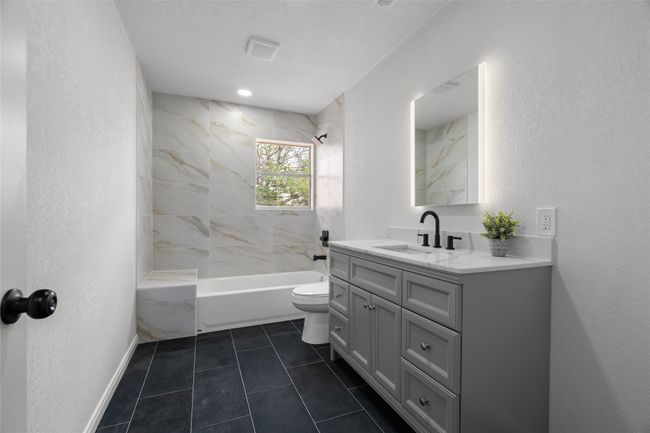 Bathroom with toilet, vanity, shower / tub combination, tile patterned floors, and a textured wall | Image 22