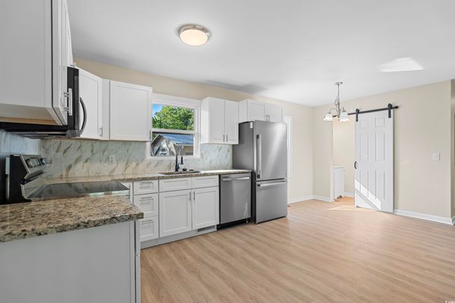 Kitchen featuring appliances with stainless steel finishes, light wood-style floors, tasteful backsplash, light stone counters, and a barn door | Image 20