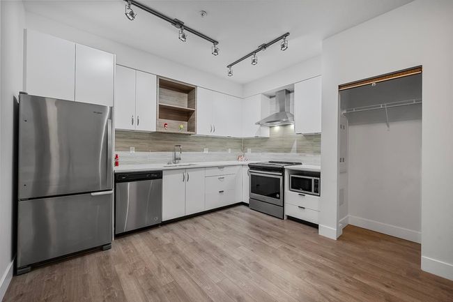Kitchen with stainless steel appliances, wall chimney exhaust hood, open shelves, light countertops, and backsplash | Image 11