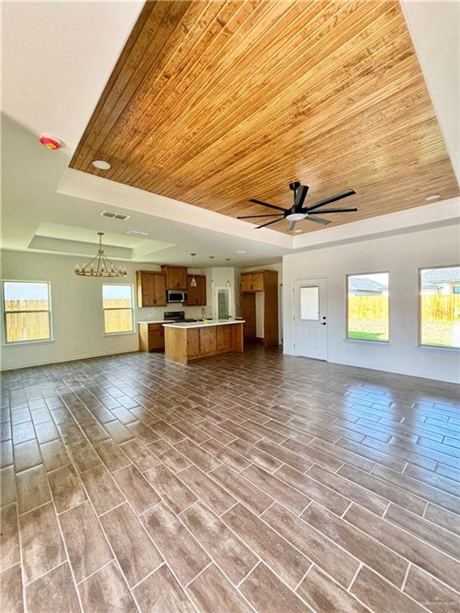 Unfurnished living room featuring visible vents, baseboards, a raised ceiling, ceiling fan with notable chandelier, and wood ceiling | Image 9